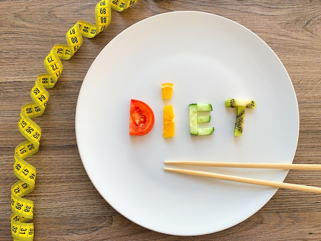 Word diet made of sliced vegetables in plate with measuring on wood background