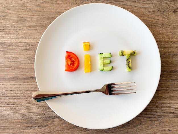 Word diet made of sliced vegetables in white plate on wood background