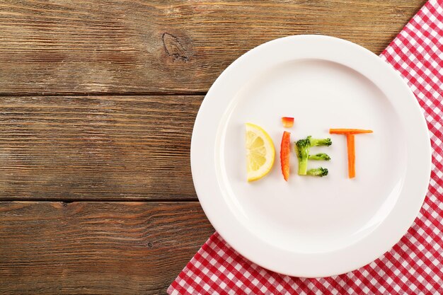 Word DIET made of sliced vegetables in white plate on wooden background