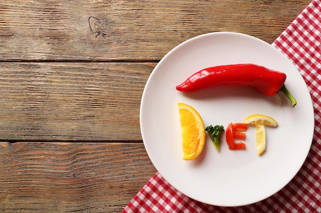 Word DIET made of sliced vegetables in white plate on wooden table top view