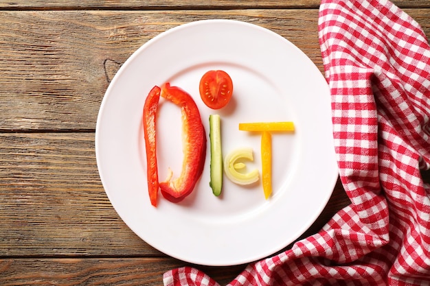 Word DIET made of sliced vegetables in white plate on wooden table top view