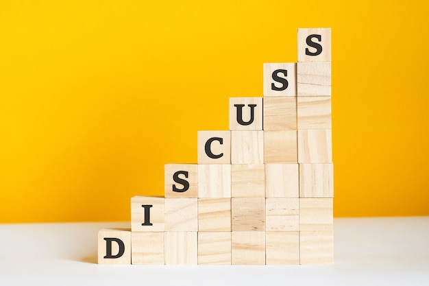 The word Discuss is written on a wooden cubes. blocks on a bright yellow background. corporate hierarchy concept and multilevel marketing. selective focus.