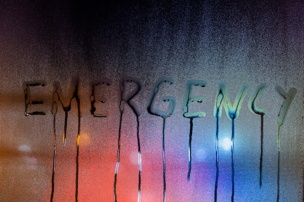 Photo the word emergency written on night wet window glass closeup with blurred background