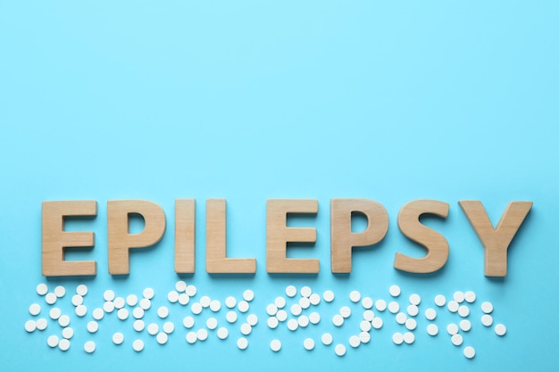 Word Epilepsy and pills on light blue background flat lay Space for text