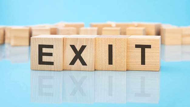 Word Exit on wooden cubes on blue background the inscription on the cubes is reflected from the surface business concept