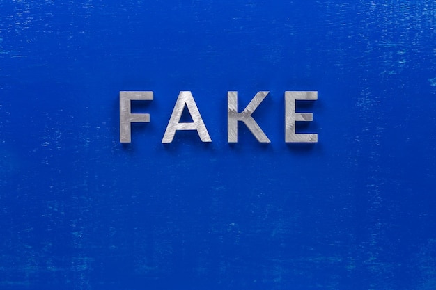 The word fake laid with silver metal characters on blue painted wooden board in central flat lay composition