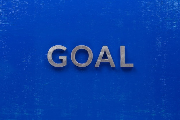 The word goal laid with silver metal characters on blue painted wooden board in central flat lay composition