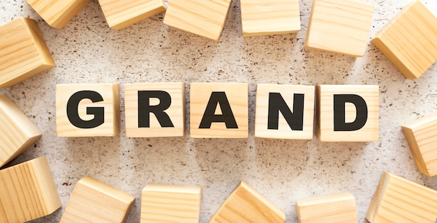 The word GRAND consists of wooden cubes with letters, top view on a light background. Work space.