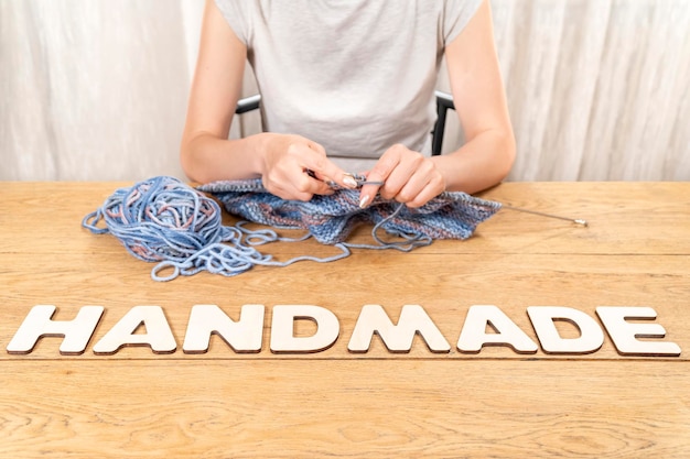 Photo word handmade is laid out in wooden letters on an old wooden table where a woman knits