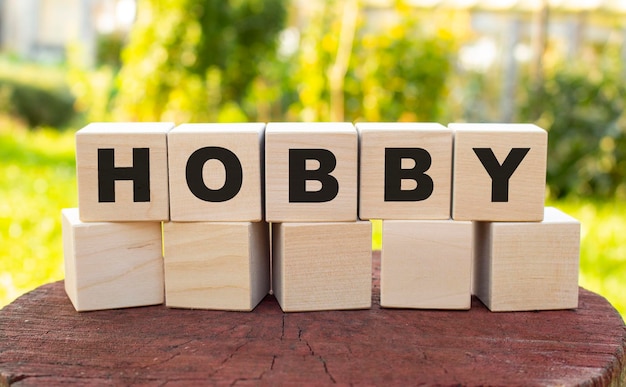 The word HOBBY is made up of wooden cubes lying on an old tree stump against a blurred garden background