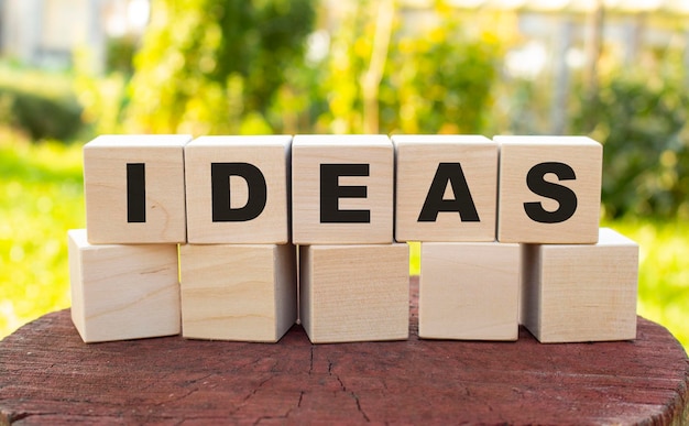 The word IDEAS is made up of wooden cubes lying on an old tree stump against a blurred garden background