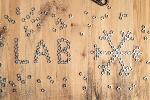 Word laboratory and a snowflake are lined with metal nuts on a wooden table. Weather forecast