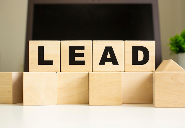 The word LEAD is written on wooden cubes lying on the office table in front of a laptop