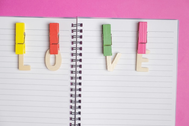 word LOVE in blank book on pink background with space for text