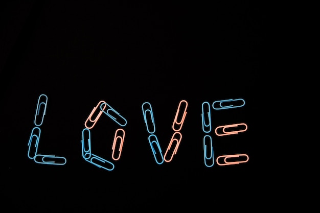 The word love is laid out from paper clips on a black background. The paper clips are pink and blue. The concept of Valentine's Day.