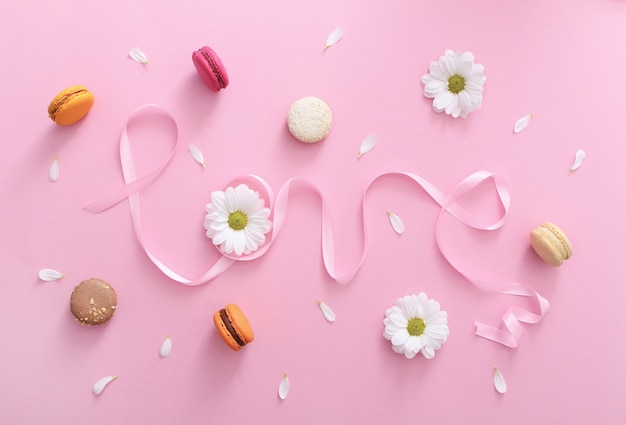 Word love made of pink ribbon with macaroons, white flowers and petals