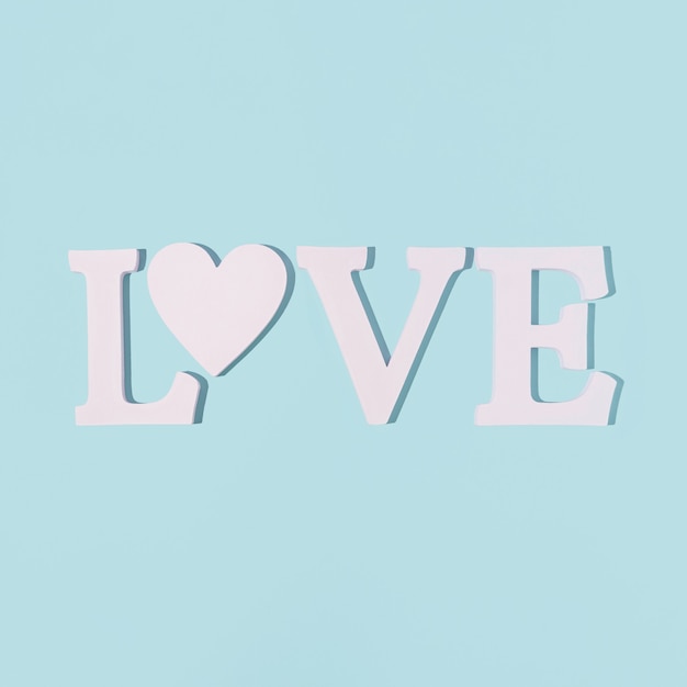 Word LOVE made with one white heart on a pastel blue background. Valentine's flat lay.