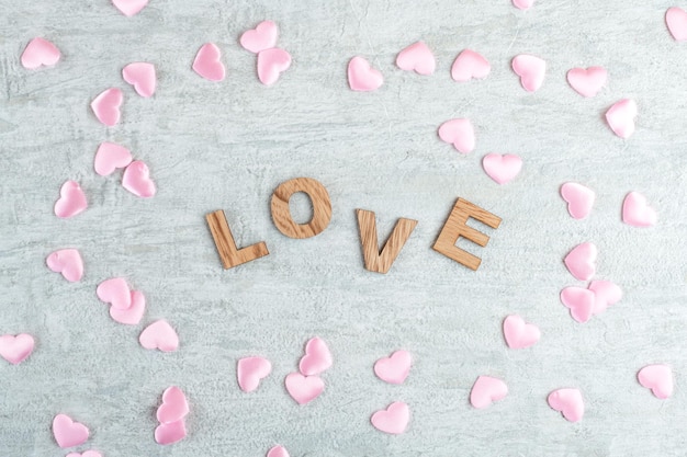 The word love in wooden letters on a light grey background with little pink hearts flat lay top view