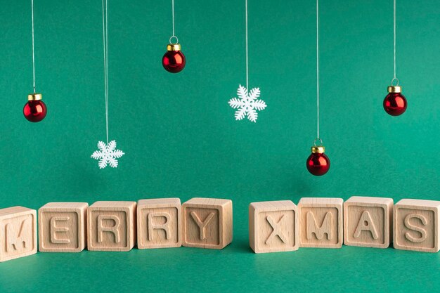 The word Merry xmas made up of wooden cubes on a green background Snowflakes and Christmas balls Christmas card