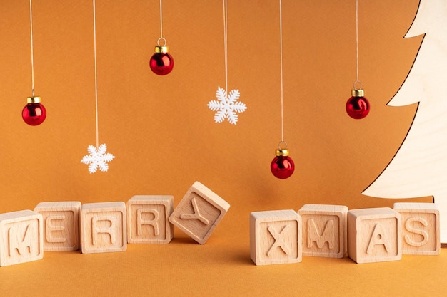 The word Merry Xmas made up of wooden cubes on an orange background Snowflakes and Christmas balls Christmas card