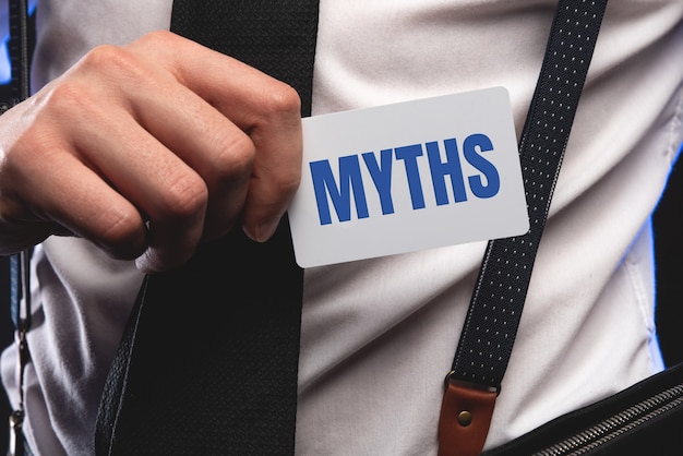 The word myths young man holding blank card against white background with vignette.