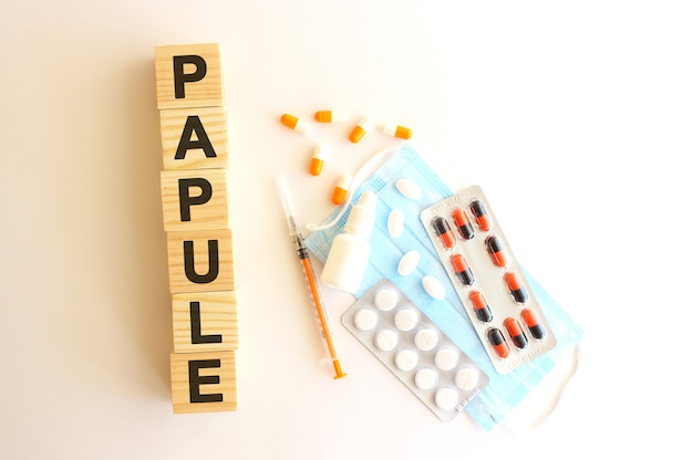 The word PAPULE is made of wooden cubes on a white surface with medical drugs and medical mask.