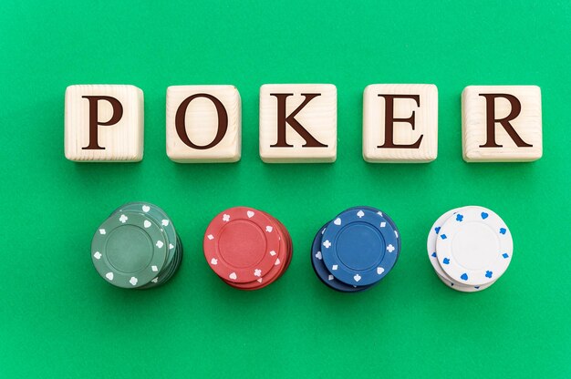 Word poker written by wooden cubes with poker chips on green casino table Top view