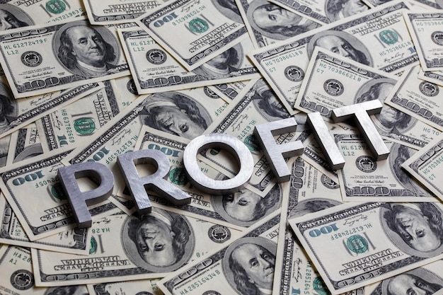 The word PROFIT laid with aluminium letters on the US dollar banknotes background with selective focus