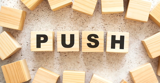 The word PUSH consists of wooden cubes with letters, top view on a light background. Work space.