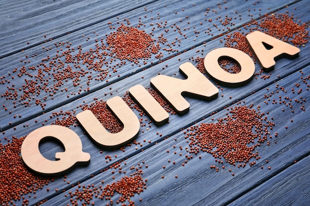 Word QUINOA made of wooden letters and seeds on table