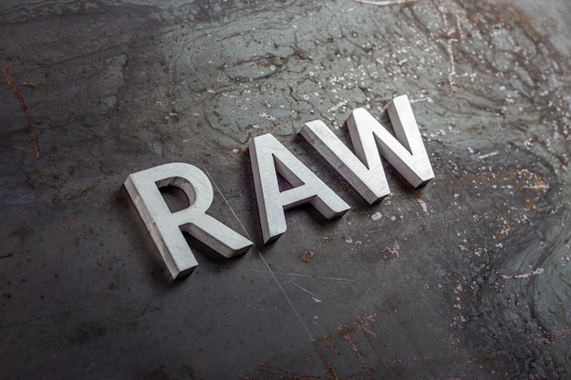 The word raw laid with silver metal letters on hot rolled steel sheet surface closeup