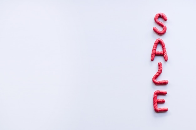 The word sale is made of plasticine red letters with white inclusions, arranged vertically, on a white background