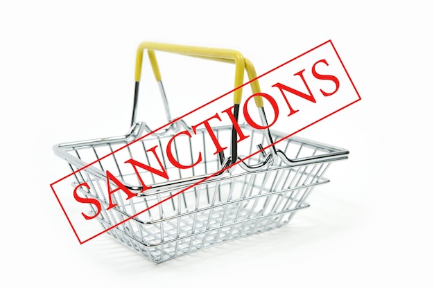 The word sanctions and an empty iron shopping basket in a supermarket on a white background is isolated