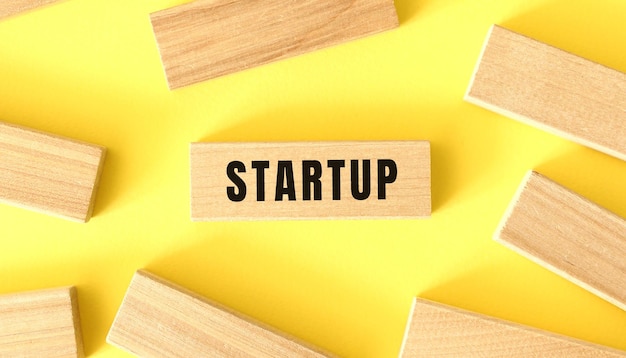 The word startup is written on a wooden blocks on a yellow background