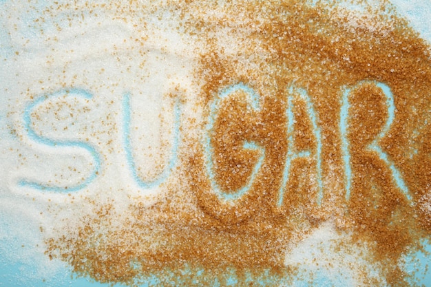 The word sugar written into a pile of white granulated sugar with blue background