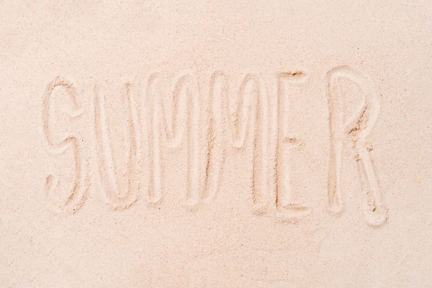 The word summer written with the finger on a sandy beach background concept of summer and holidays copy space