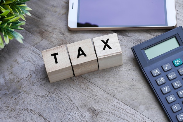 Word Tax on small wooden cubes with a calculator, a smartphone on a wooden table