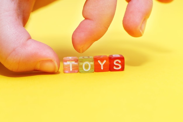 Word toys with colorful cubes of beads and child's hand on yellow background