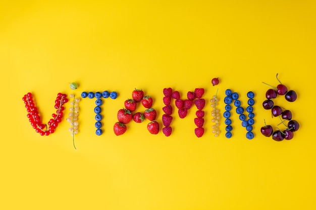 The word Vitamins made of different fresh summer berries on a yellow background