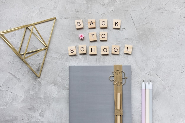 Words BACK TO SCHOOL notebook and pens on a gray background