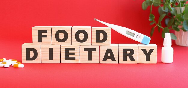 The words FOOD DIETARY is made of wooden cubes on a red background with medical drugs.