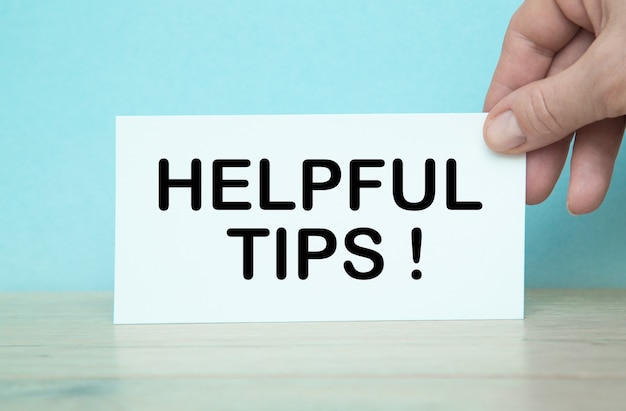 The words HELPFUL TIPS written on the notebook. Notebook in hand on a blue background.