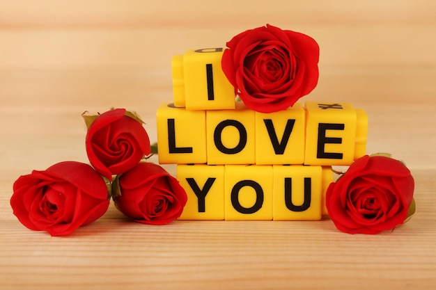 Words I Love You formed from cubes with flowers on wooden background