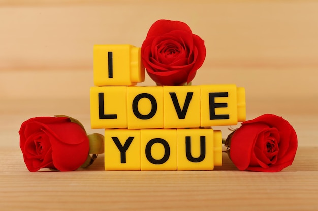 Words I Love You formed from cubes with flowers on wooden background