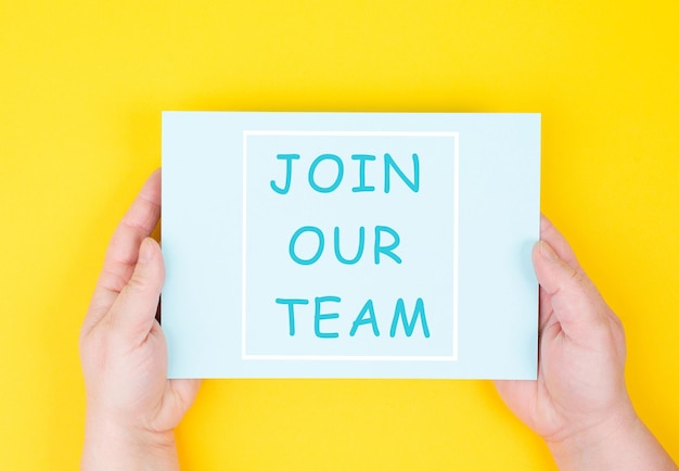 Photo the words join our team are standing on a paper, yellow colored background, hands hold message