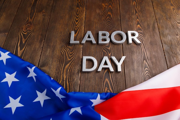 Words labor day laid with silver metal letters on wooden surface with crumpled usa flag on bottom