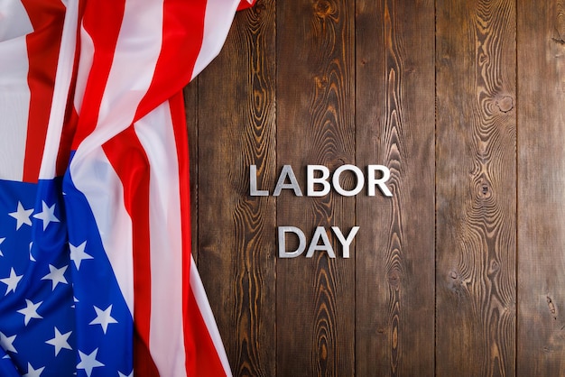 Words labor day laid with silver metal letters on wooden surface with crumpled USA flag on left side