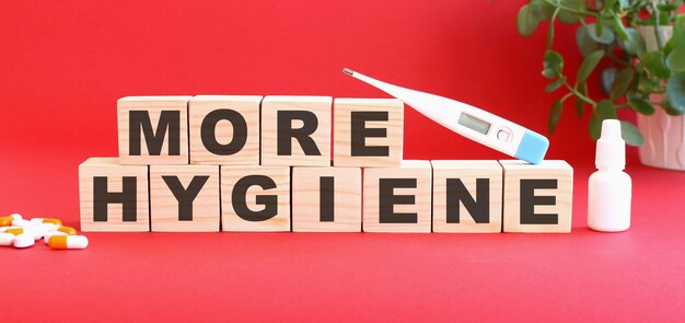 The words MORE HYGIENE is made of wooden cubes on a red background with medical drugs.