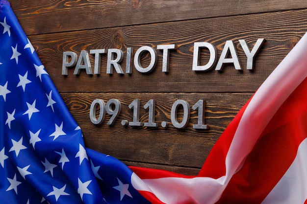 words patriot day laid with silver metal letters on wooden board surface with crumpled US flag