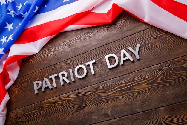 The words patriot day laid with silver metal letters on wooden board surface with crumpled usa flag